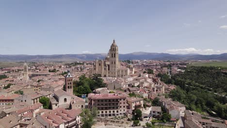 Aerial-view-orbiting-Segovia-Roman-catholic-cathedral,-Plaza-Mayor-scenic-medieval-cityscape-and-mountain-skyline