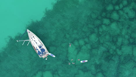Aerial-View-People-Swimming-In-the-Clear-Water-near-The-Sailboat