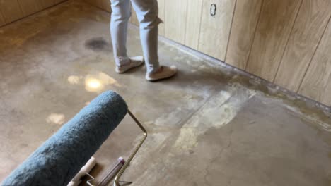 Painting-doing-home-improvement-diy-remodel-of-basement-with-light-wood-panels-and-concrete-floor-painting-bright-white-husband-and-wife-team-couple-male-painters-pov-perspective---in-4K-60fps