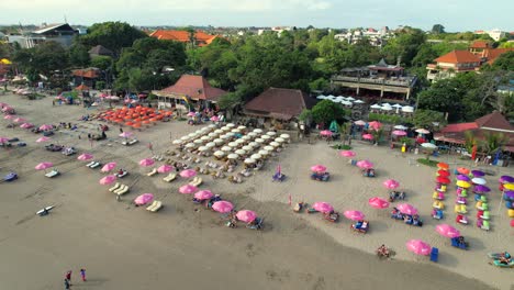 Flying-Over-Double-Six-Beach-Packed-with-Rental-Umbrellas-in-Peak-Summer-Season-in-Seminyak,-Bali,-Indonesia