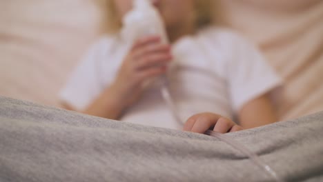 Verschwommenes-Mädchen-Atmet-Mit-Inhalator-Im-Bett,-Fokus-Auf-Kinderhand