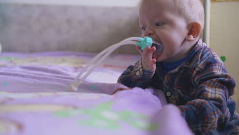 funny-baby-in-checkered-shirt-plays-with-aspirator-at-bed