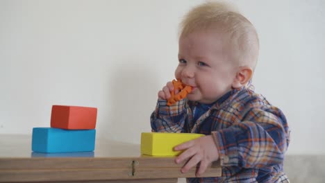 Fröhliches-Baby-Knabbert-An-Einem-Orangefarbenen-Teil-Am-Niedrigen-Holztisch-In-Nahaufnahme
