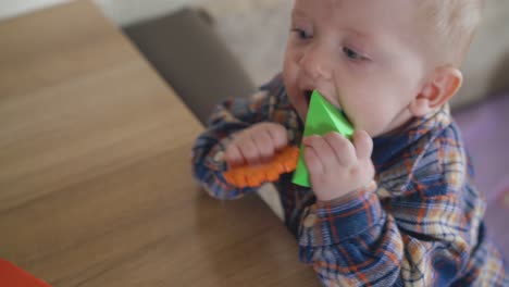 Baby-Knabbert-An-Weichem-Gummispielzeug-Und-Lehnt-An-Einem-Niedrigen-Holztisch