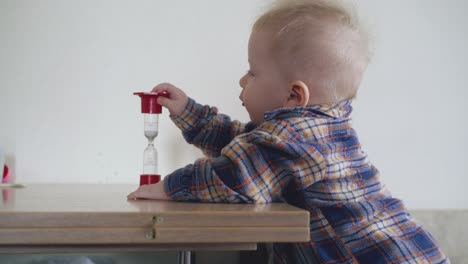 mother-gives-sandglass-to-cute-baby-leaning-on-low-table