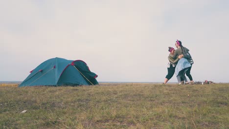 girl-hikers-dance-hugging-at-campsite-on-green-meadow