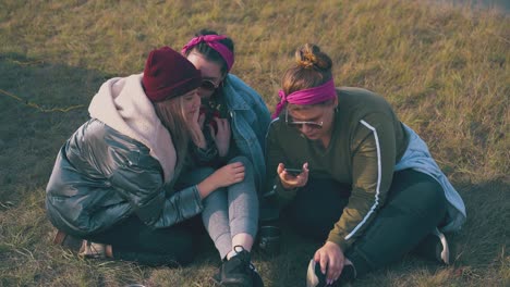 Mädchentouristen-Schauen-Sich-Auf-Dem-Gras-Sitzend-Ein-Video-Auf-Dem-Smartphone-An
