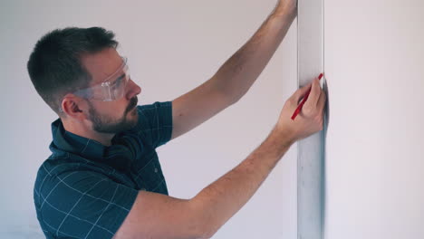bearded-man-checks-wall-angle-using-level-and-pencil-in-room