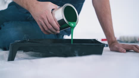 man-pours-green-paint-into-plastic-tray-on-floor-closeup