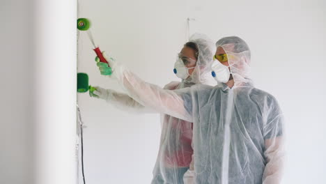 man-and-woman-in-transparent-coveralls-paint-room-white-wall