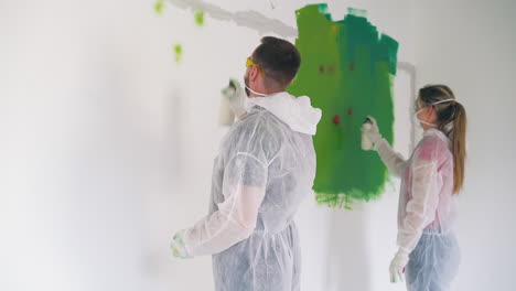 guy-and-girl-in-transparent-coveralls-paint-wall-with-sprays