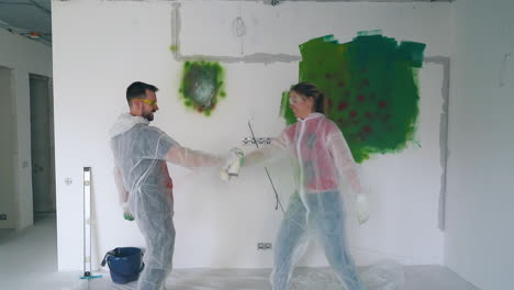 joyful-guy-and-girl-fight-with-spray-paints-and-kiss-in-room