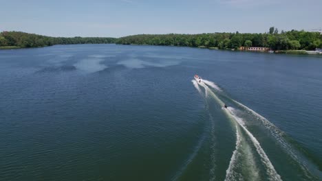 Motorboat-pulling-waterski-on-a-lake-in-the-forest,-drone-shot