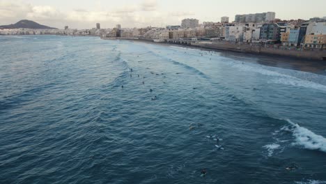Cinematic-shot-of-surfers-in-the-waters-of-Las-Canteras-Beach-in-Las-Palmas-de-Gran-Canaria,-Drone,-Aerial