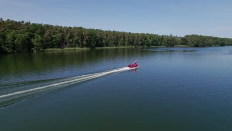 Boy-holds-polish-national-flag-on-front-of-the-red-motorboat,-epic-following-drone-shot