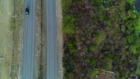 Top-down-drone-follows-highway-road-on-tropical-hillside,-bird's-eye-view