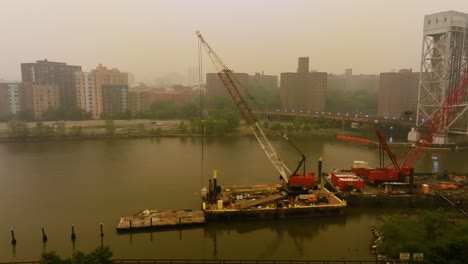 Drone-shot-toward-a-harbor-crane-at-the-Harlem-river,-hazy-day-in-New-York,-USA