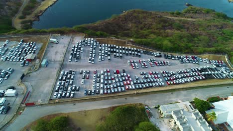 White-and-black-cars-parked-in-industrial-transport-import-export-lot,-aerial-rise-tilt-down
