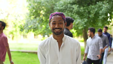 Close-up-portrait-of-a-Pakistani-male-student-smiling,-standing-alone-on-campus,-and-looking-at-the-camera
