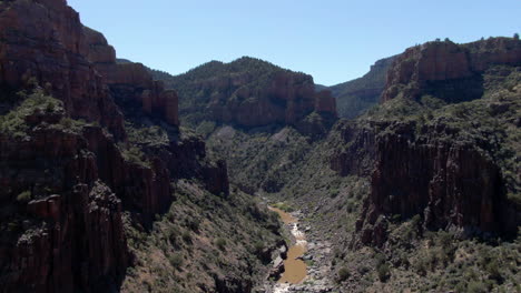 Aerial-view-following-a-river,-in-middle-of-a-towering-canyon-walls,-in-AZ,-USA