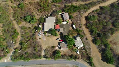 Drone-rises-from-ramshackle-homes-in-dry-arid-vegetation,-aerial-top-down