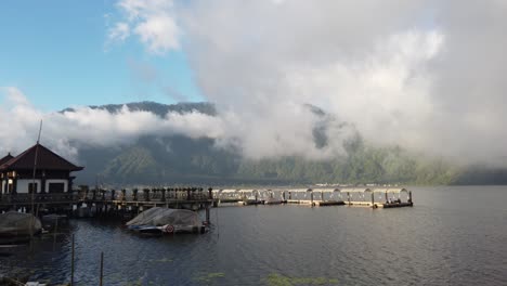 Lago-Beratan-En-Bali,-Indonesia,-Cuando-Las-Nubes-De-Tormenta-Y-La-Niebla-Comienzan-A-Despejarse-Y-El-Sol-Se-Abre-Paso-Revelando-Montañas-En-El-Fondo
