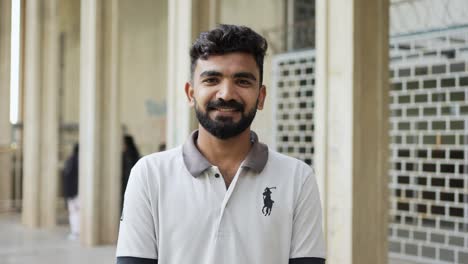 Nahaufnahmeporträt-Eines-Pakistanischen-Männlichen-Studenten,-Der-Lächelt,-Allein-Auf-Dem-Campus-Steht-Und-In-Die-Kamera-Schaut