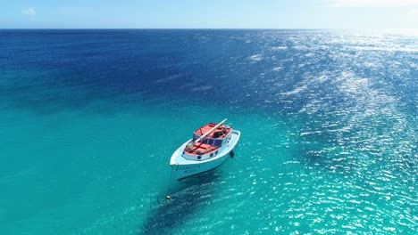 Drone-rises-above-wooden-fishing-yacht-in-middle-of-Caribbean-ocean-casting-shadow-on-clear-sandy-water-below