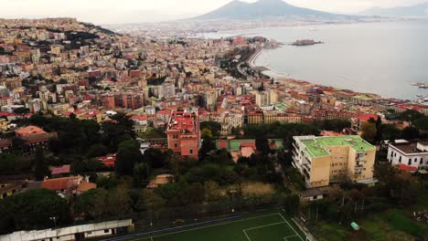 Aerial-flyover-suburb-area-of-Naples-with-soccer-field-on-hilltop-and-Beautiful-cityscape-in-the-valley-along-coastline