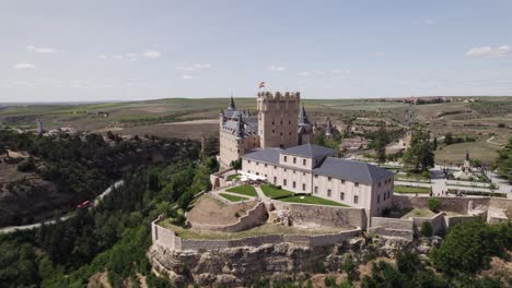 Aerial-view-circling-the-Alcazar-of-Segovia-medieval-castle-fortress-standing-on-top-of-rocky-crag-overlooking-Spanish-old-city-landscape