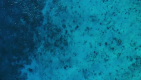 crystal-clear-turquoise-Caribbean-sea-drop-off-to-deep-blue-coral,-drone-rising,-bird's-eye-view