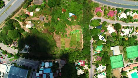 Drone-top-down-static-shot-above-farm-field-surrounded-by-homes-and-development,-cloud-shadow-passes-over