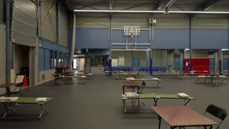 Flüchtlingsunterkunft-Auf-Basketball-Sporthalle,-Bett-Und-Tisch-In-Einer-Reihe,-Dolly-Shot