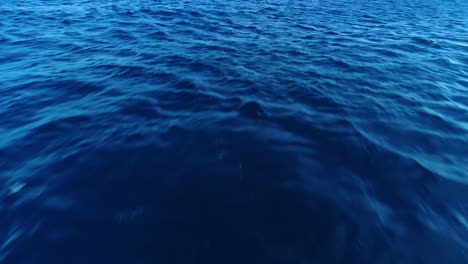 Deep-blue-ocean-water-view-from-surface-as-ripples-and-waves-blow-across-top,-ocean-texture
