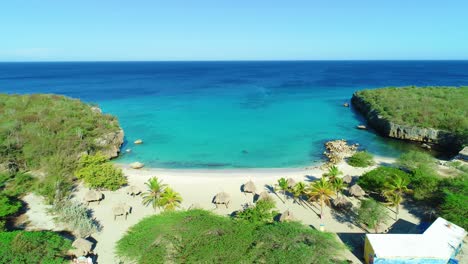 Hidden-Caribbean-sandy-beach-cove-bay-with-beachside-huts-at-Daaibooi-beach-in-Curacao,-aerial