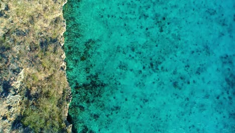 Drone-top-down-trucking-pan-along-cliffside-edge-and-clear-blue-ocean-water-reef
