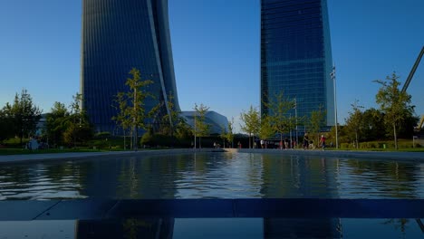 Las-Tres-Torres-De-La-Vida-Urbana-Del-Distrito-De-Lombardía-En-Milán,-Italia,-Se-Reflejan-En-La-Fuente-Debajo-De-Ellas.