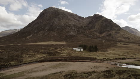 Aerial-of-Lagangarbh-Hut-white-cottage-in-Glencoe-Scottish-Highlands-with-mountain-Buachaille-Etive-Mor-in-the-distance