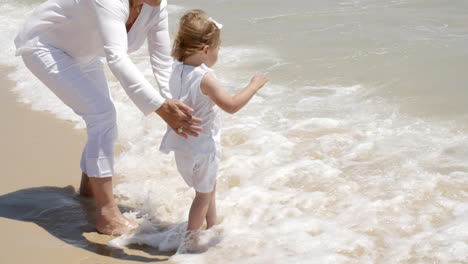 Mutter-Hält-Ihr-Mädchen-Am-Strand-Planschen-Wasser