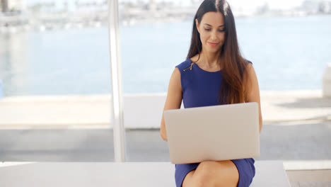 Woman-sitting-on-a-waterfront-bench-using-a-laptop