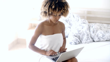 Happy-woman-using-laptop-on-bed.