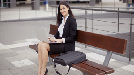 Frau-Schaut-Mit-Laptop-Auf-Bank-Herüber