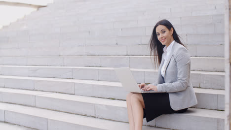 Smiling-woman-using-laptop-on-stairs