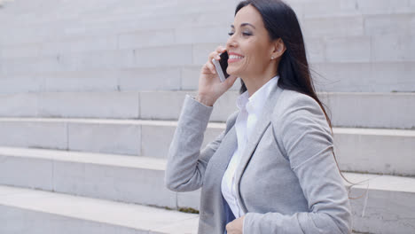 Lachende-Frau-Sitzt-Auf-Der-Treppe-Mit-Telefon