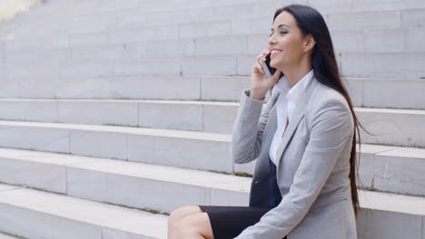 Lachende-Frau-Sitzt-Auf-Der-Treppe-Mit-Telefon