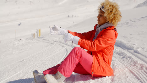 Frau-Im-Orangefarbenen-Schneeanzug-Sitzt-Auf-Der-Skipiste