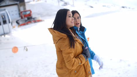 Two-young-women-walking-through-snow-at-a-resort