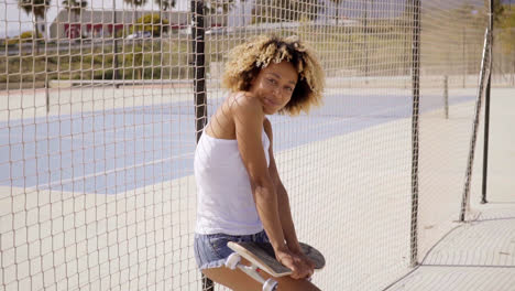 Junge-Frau-Mit-Skateboard-Lehnt-Sich-Gegen-Zaun