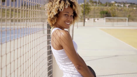 Young-woman-with-skateboard-leans-against-fence