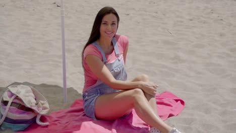 Young-woman-waving-hand-while-on-beach-blanket